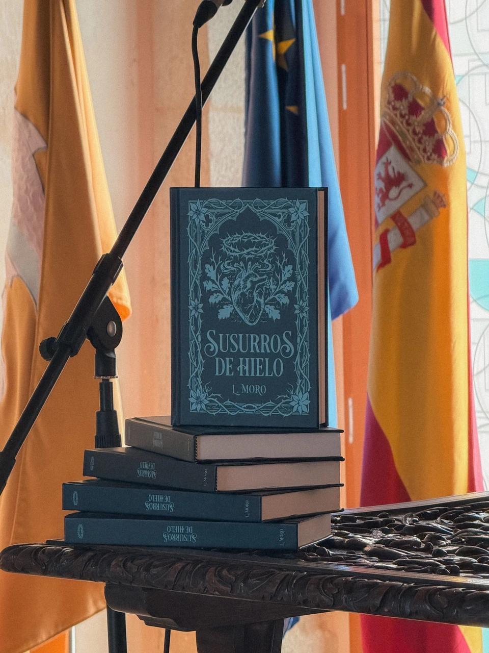 Copies of Susurros de Hielo stacked on a carved table beside a microphone.