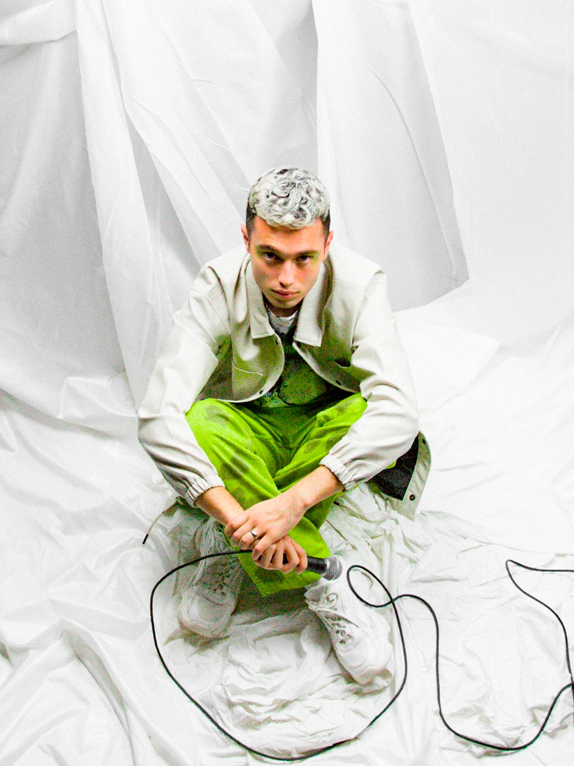 Behind-the-scenes portrait of Víctor Recio Rodríguez seated on white fabric during the vicxvers production.