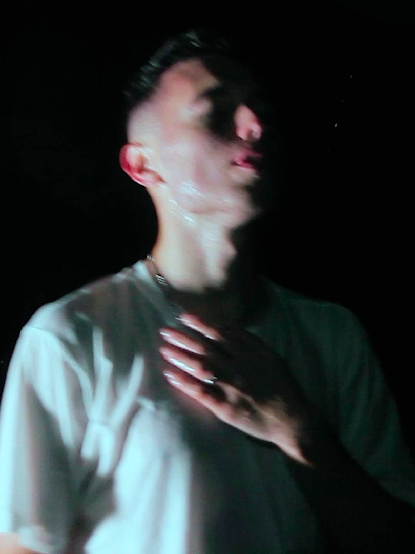 Blurred low-light still of Víctor Recio Rodríguez performing in a white T-shirt.