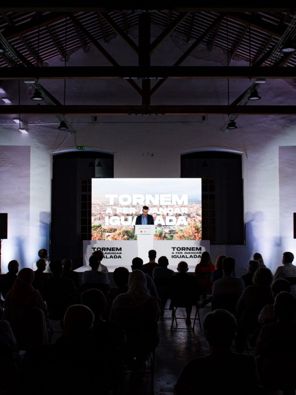 Audience facing the stage at an Igualada Som-hi event inside an industrial hall.