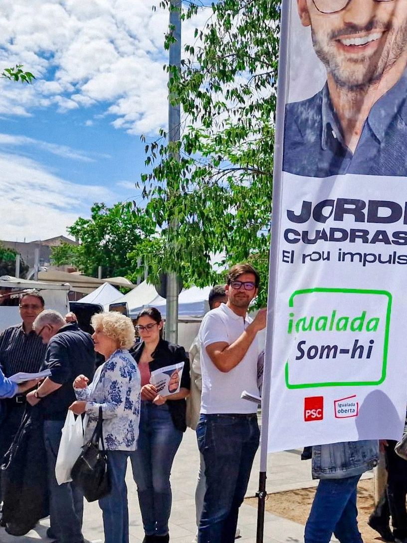 Campaign conversations in a public square beside a Jordi Cuadras banner.