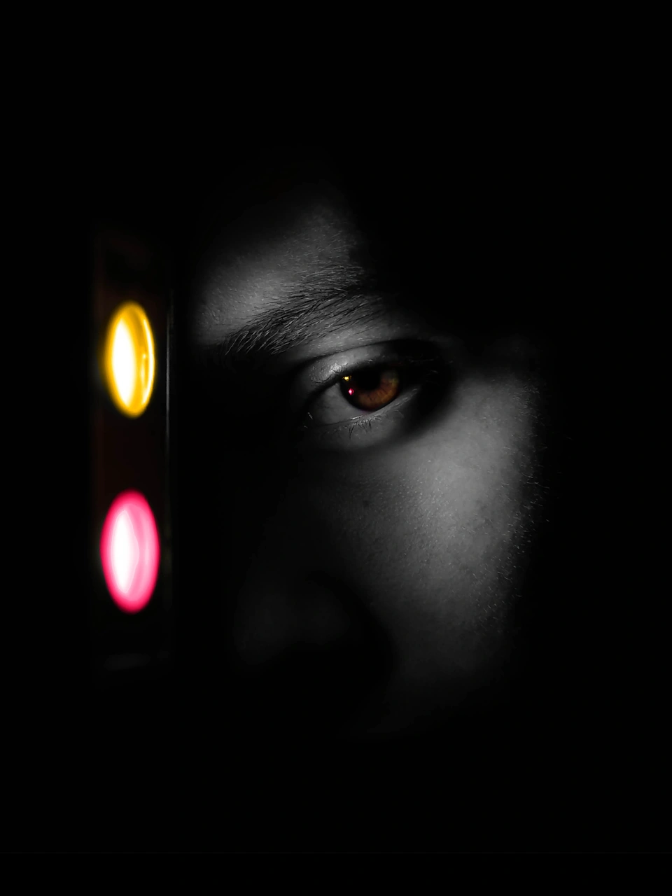 Dark samemess portrait with yellow and pink lights beside the face.